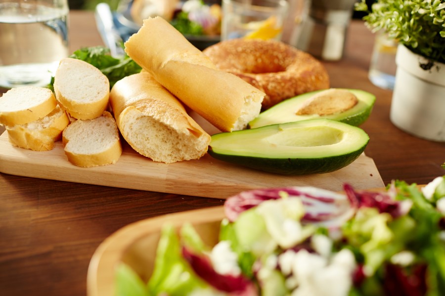 Brot und Avocado auf einem Holzbrett, mit Salat im Vordergrund.