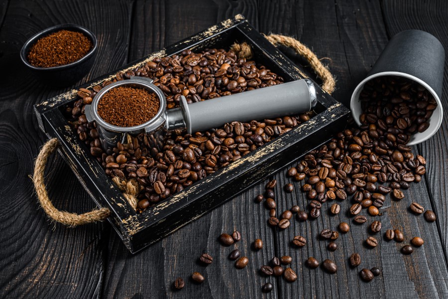 Kaffeebohnen und gemahlener Kaffee mit Siebträger auf dunklem Holz.