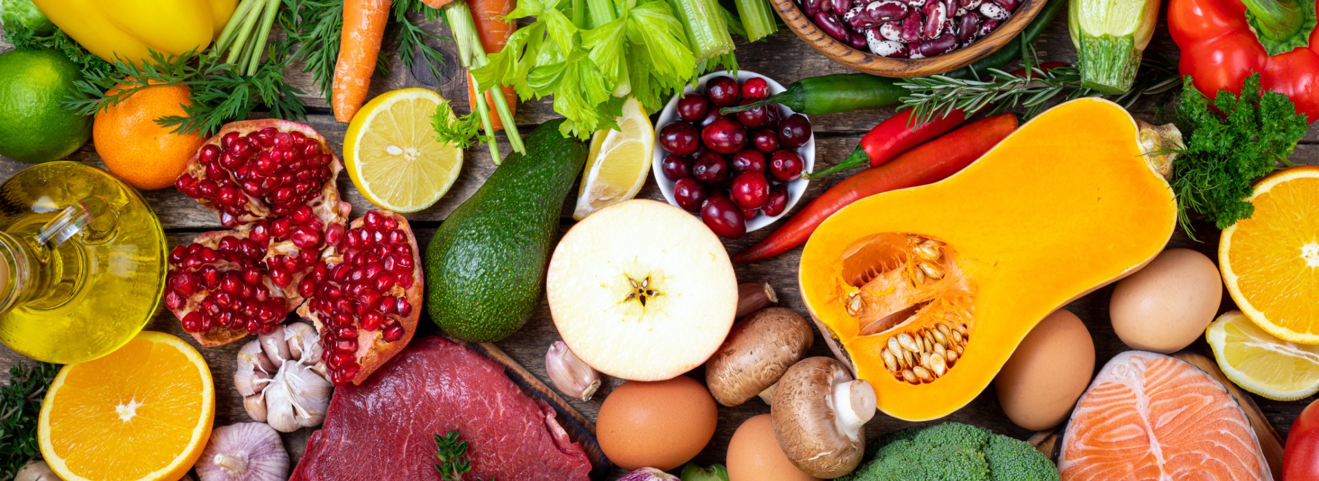 Bunte Auswahl an frischen Lebensmitteln: Obst, Gemüse, Fleisch, Fisch, Eier und Öl auf Holztisch.