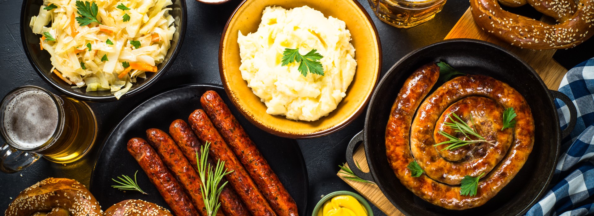 Deftiges Essen mit Bratwürsten, Kartoffelpüree, Krautsalat, Brezeln und Bier.
