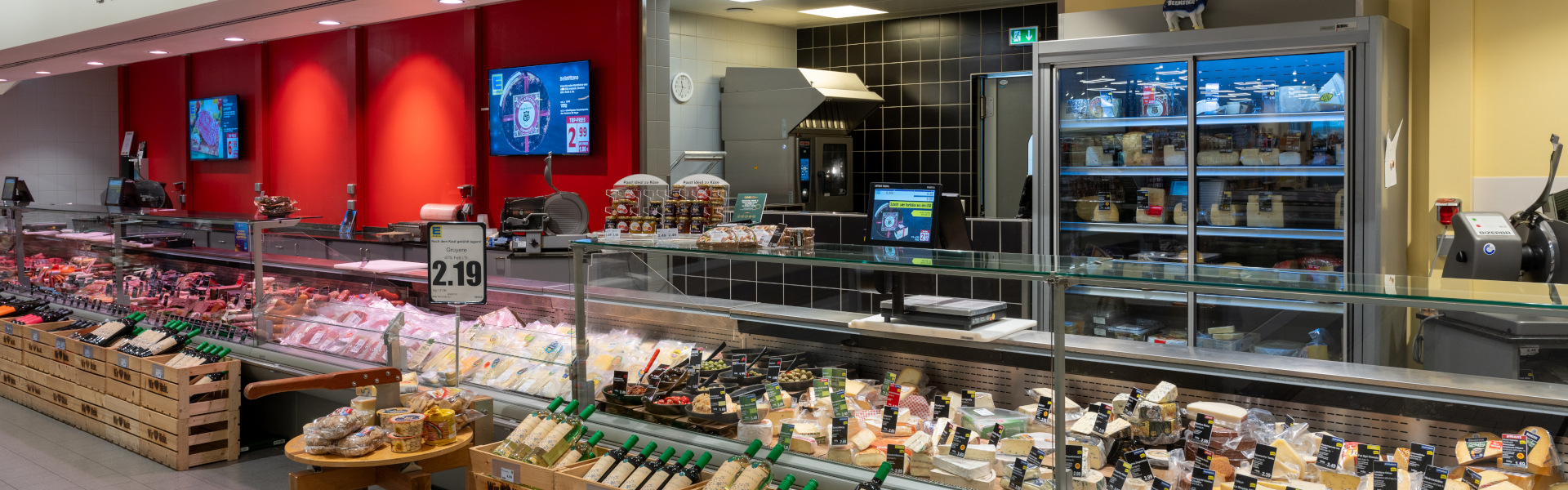 Käse- und Wursttheke im Supermarkt mit Kühlvitrinen und Arbeitsbereich dahinter.