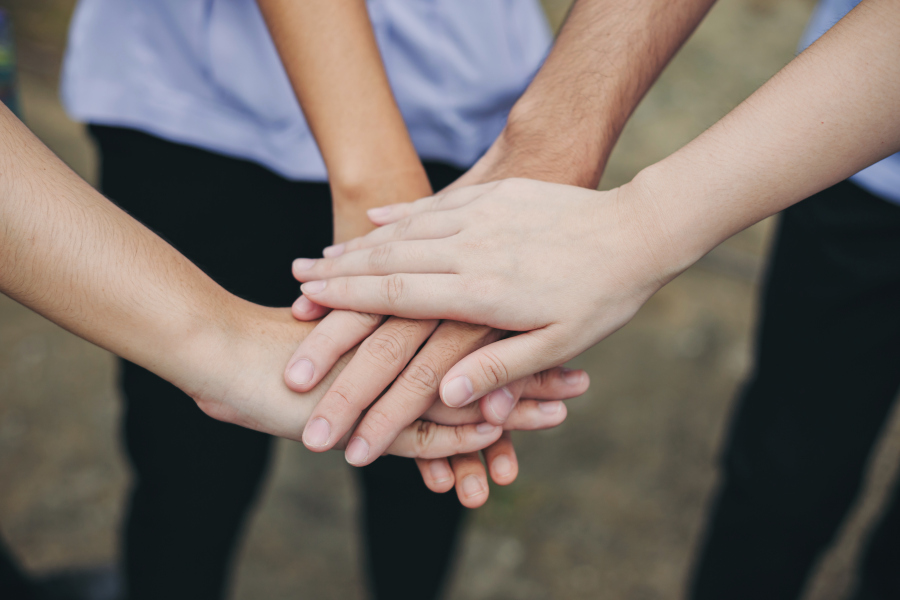 Mehrere Hände übereinander als Symbol für Teamwork und Zusammenhalt.