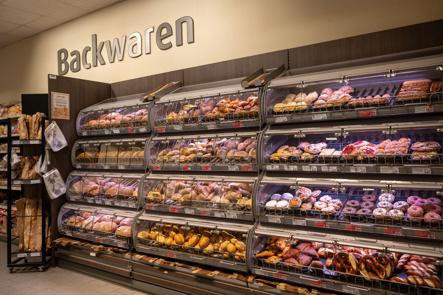 Backwaren-Regal im Supermarkt mit Broten, Brötchen und süßem Gebäck.