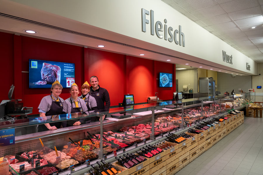 Metzgereitheke im Supermarkt mit Fleisch-Auslage und Mitarbeitenden hinter der Theke.