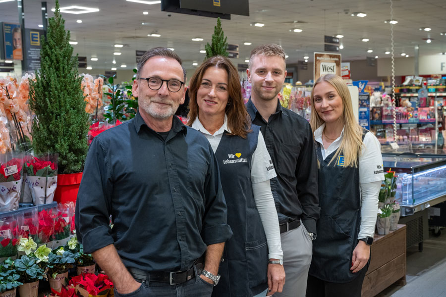 Vier Supermarkt-Mitarbeitende posieren im Markt zwischen Pflanzen und Warenregalen.